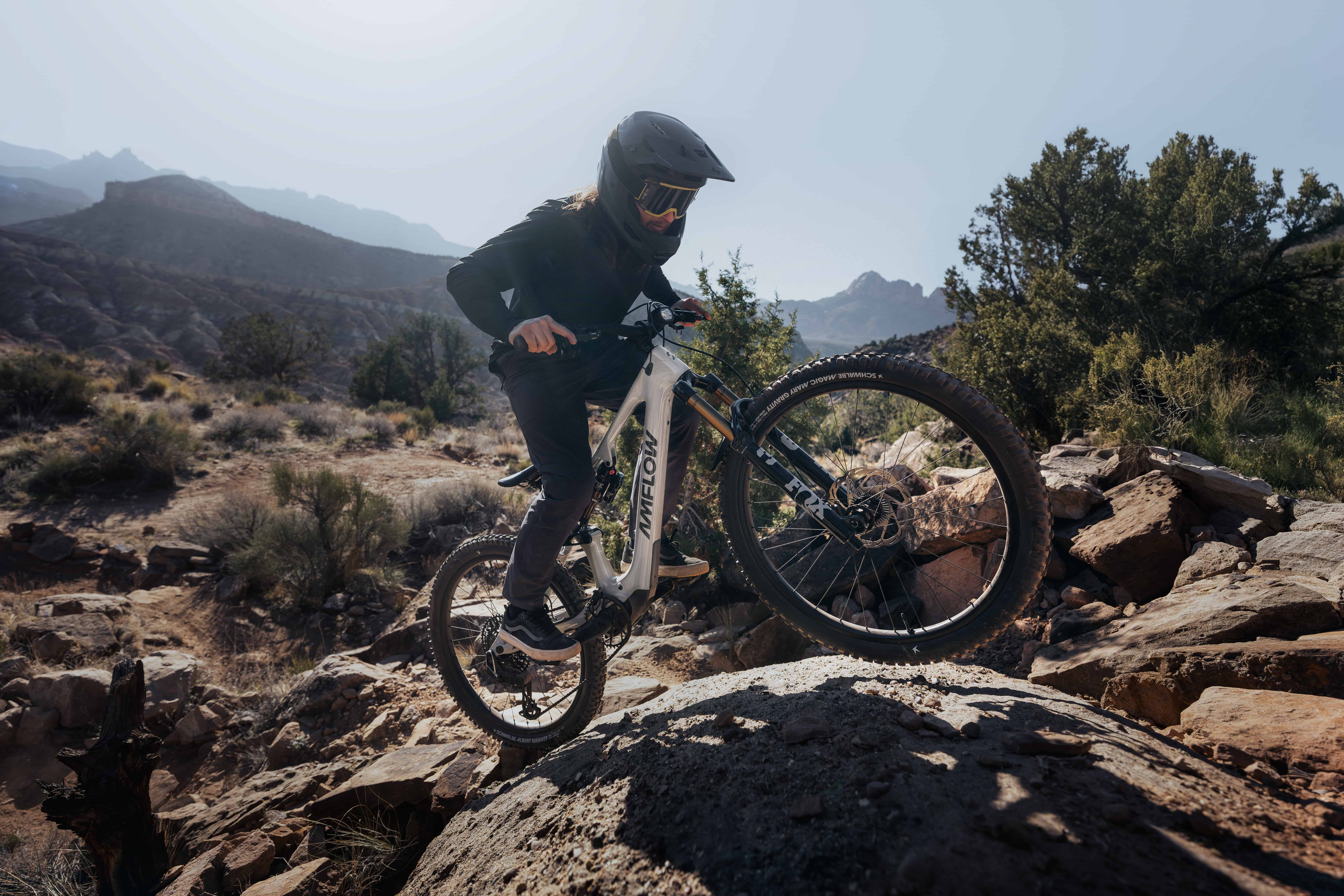 Mountain biker riding an electric mountain bike up a steep, rocky trail in rugged terrain.